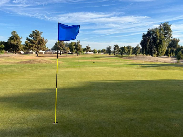 Blue flag on a putting green overlooking open fairways and trees at Lemoore Golf Course in Lemoore, CA.